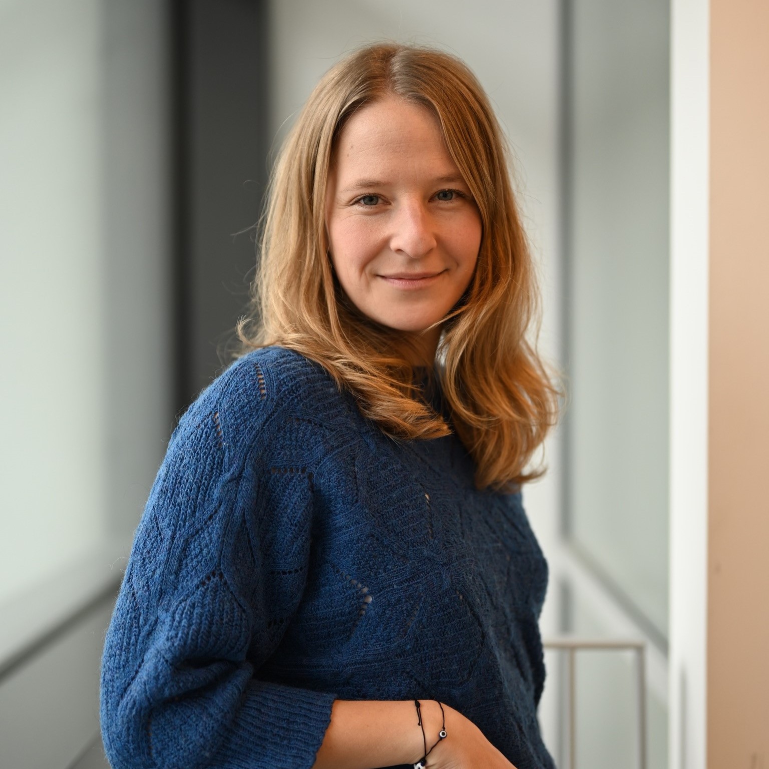 Elisabeth steht in einem hellen Flur, sie lehnt sich an eine Brüstung